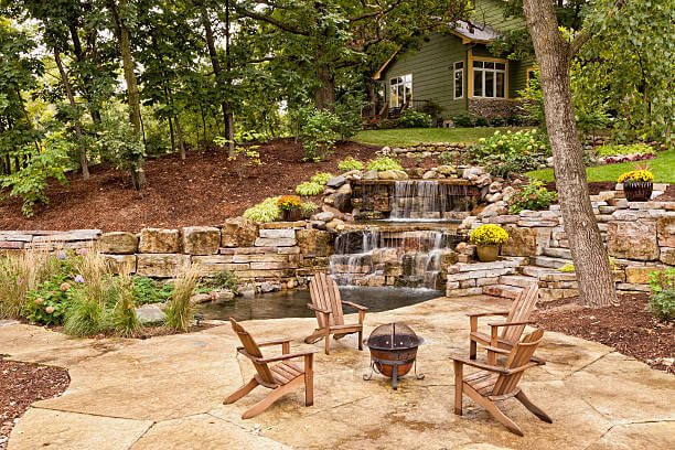 Beautiful landscaping with waterfall, koi pond, and stone patio with wooded surroundings.