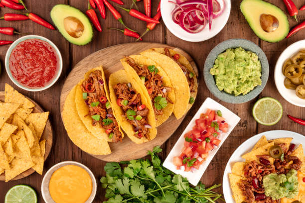 An overhead photo of an ssortment of many different Mexican tapas, including tacos, guacamole, pico de gallo, nachos and others